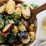 A bowl of no mayo potato salad with a wooden spoon dipping into it.