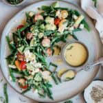 Asparagus salad on a grey plate. There is a small bowl of dressing to the side.