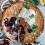 Berry cobbler baked in a round dish with a portion missing and two scoops of ice cream on top.