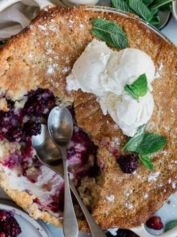 Berry cobbler baked in a round dish with a portion missing and two scoops of ice cream on top.