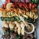 Steak kabobs and vegetable skewers on a platter with a bowl of marinade with a brush.