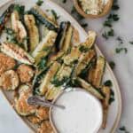 A platter of air fryer zucchini with a bowl of parmesan cheese on the side and a creamy white sauce.