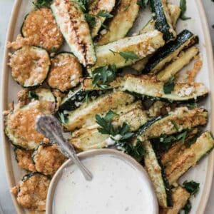 Air fryer zucchini on a platter with a bowl of ranch.