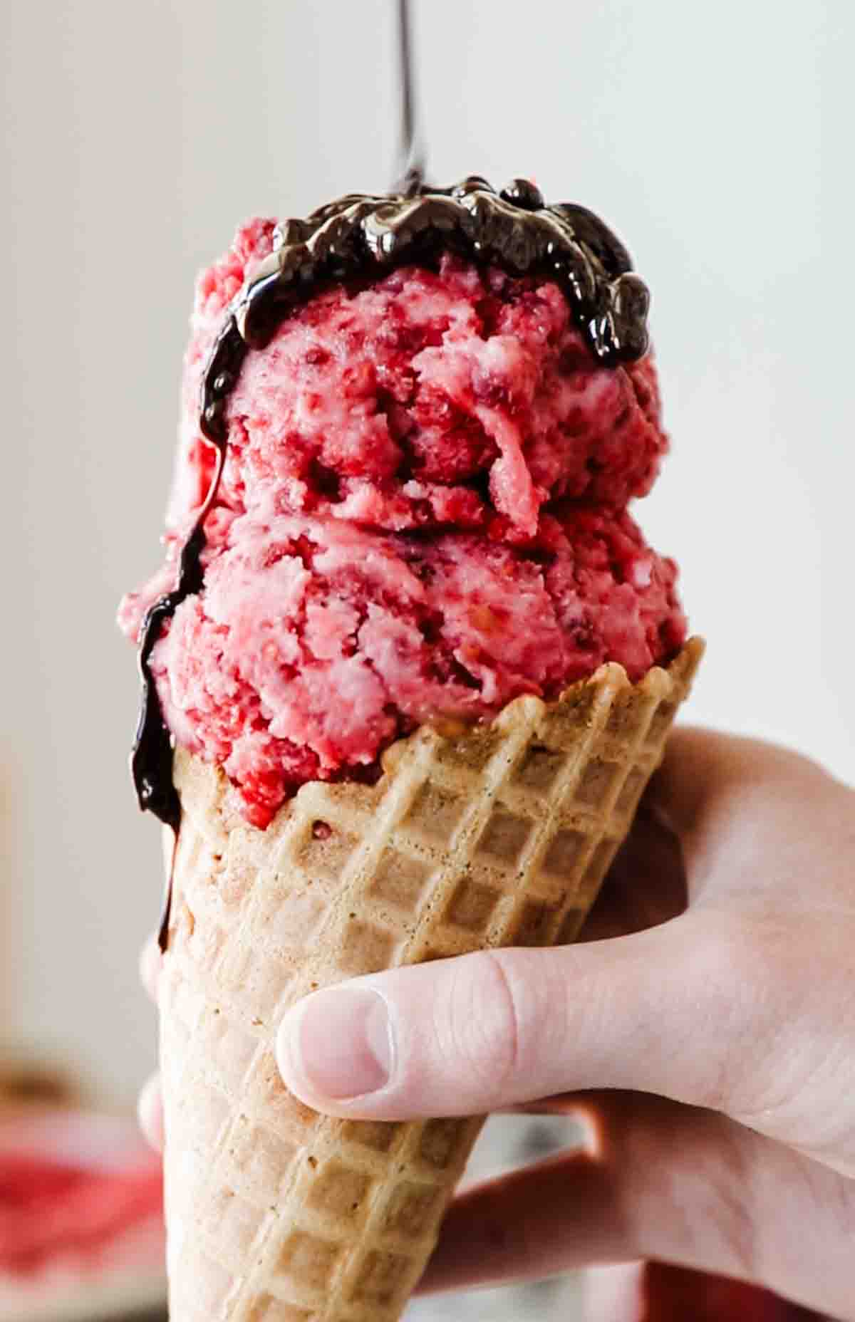A hand holding a cone filled with raspberry ice cream sorbet.