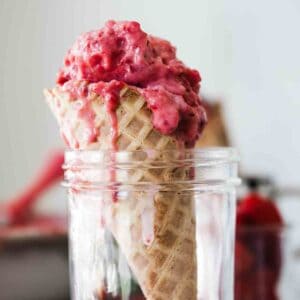 A raspberry ice cream cone in a jar on the table with a loaf pan full of it in the background.