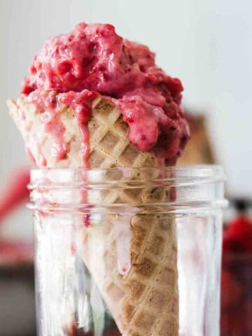 A raspberry ice cream cone in a jar on the table with a loaf pan full of it in the background.