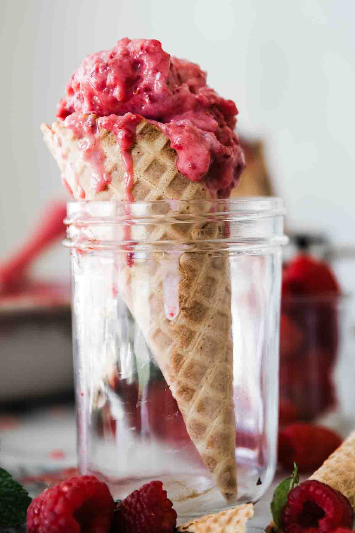 A raspberry sherbet ice cream cone in a glass jar on the table.