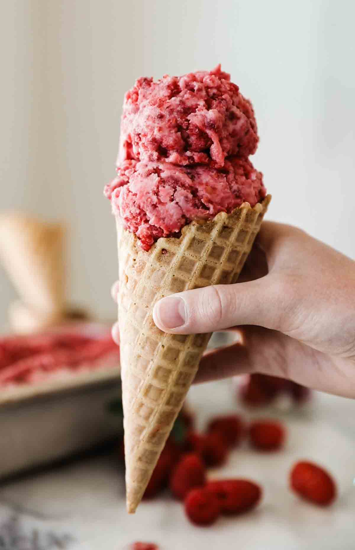 A hand holding a raspberry sherbet ice cream cone. 