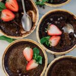 Four ramekins of chocolate creme brulee topped with mint and strawberries.