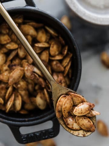 A bowl of air fryer pumpkin seeds with a spoon holding some over the dish.