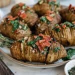 Hasselback potatoes on a platter topped with herbs and bacon.