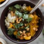 Pumpkin curry in a black bowl with cilantro and peanuts on top.