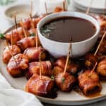 Bacon wrapped water chestnuts on a plate around a bowl of sauce.