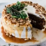 An easy carrot cake with a slice missing on a white cake stand.