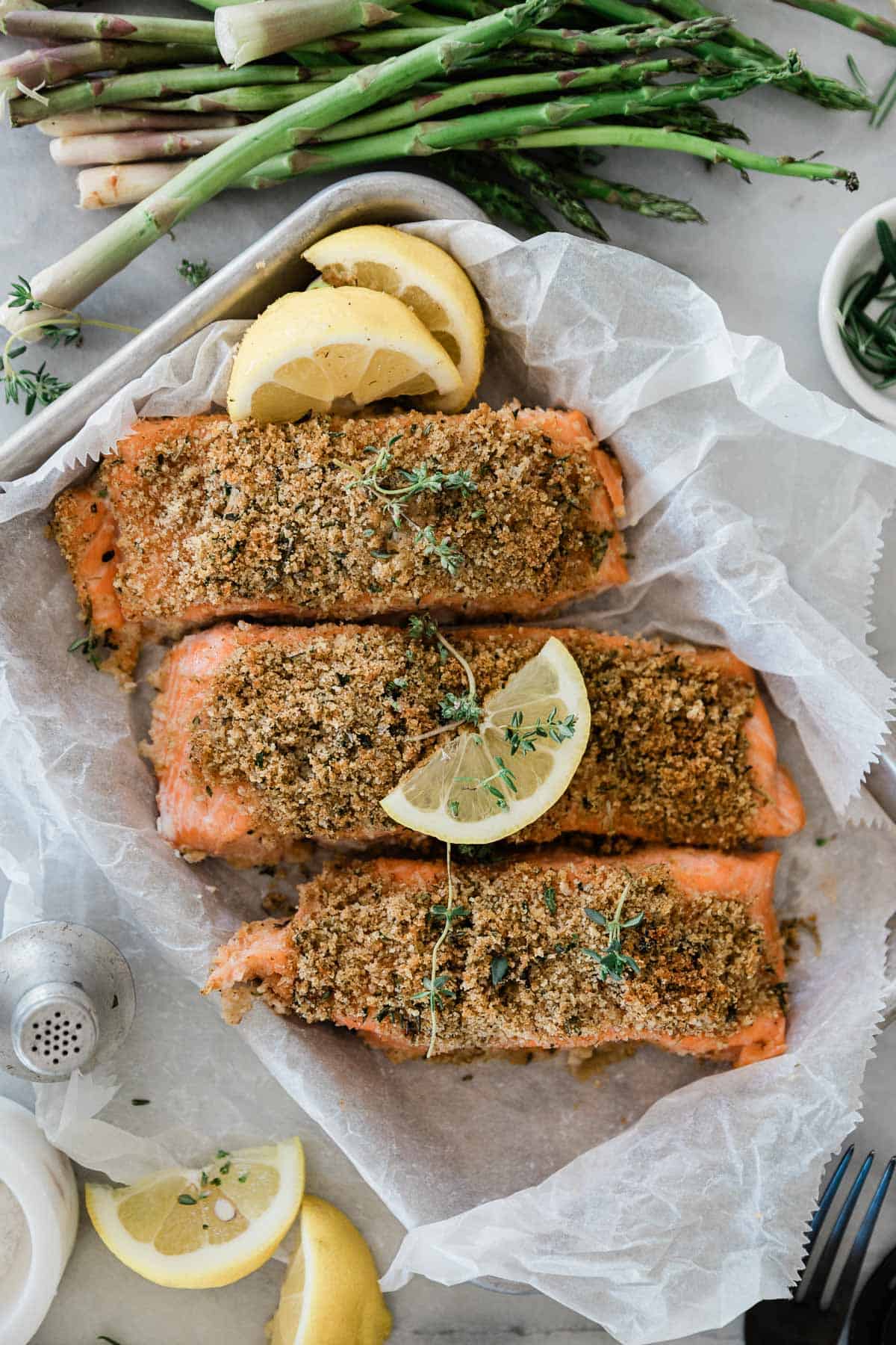 Herb crusted salmon on a baking tray with lemon slices.