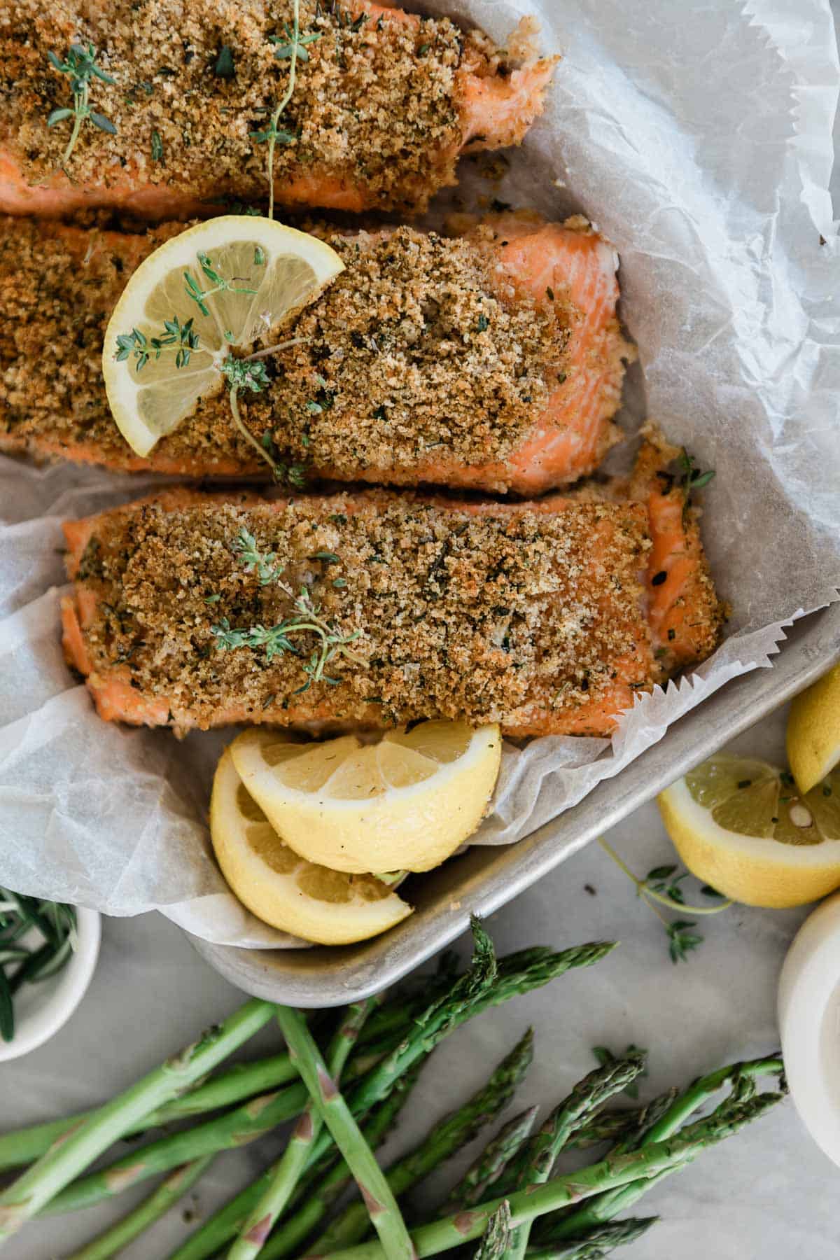 A few pieces of baked panko salmon on a pan with lemon slices.