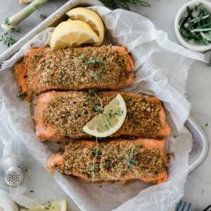 Three pieces of herb crusted salmon on a baking pan garnished with lemons.