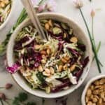 Peanut coleslaw in a bowl with herbs around on the table.