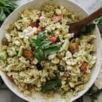 A bowl of healthy pasta salad with a wooden spoon in it to serve.