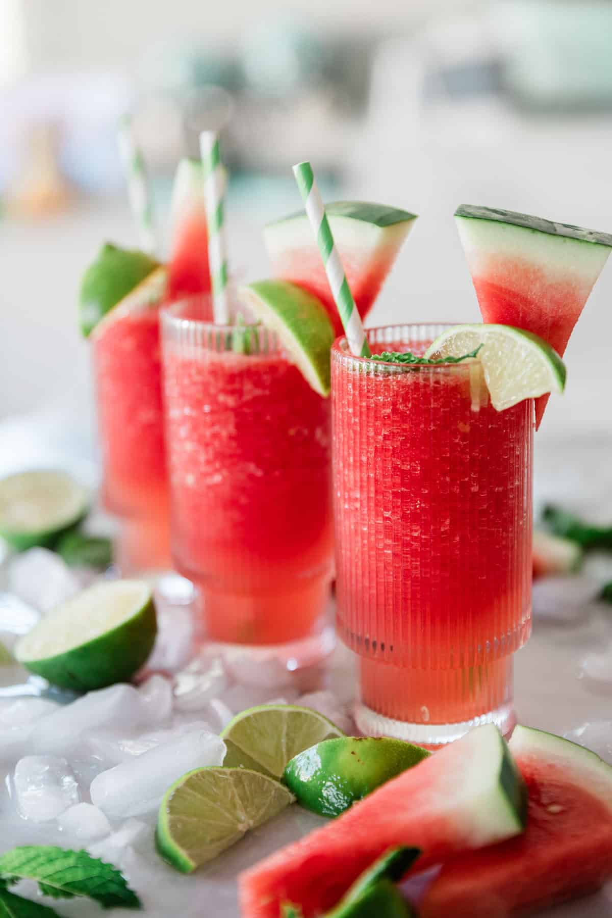 Three glasses of watermelon slushie garnished with lime, watermelon, and a straw.
