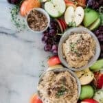Bowls of cream cheese apple dip on a marble block with fruit and nuts.