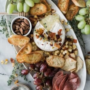 Baked brie appetizer on a white oval platter with fruit and crackers.