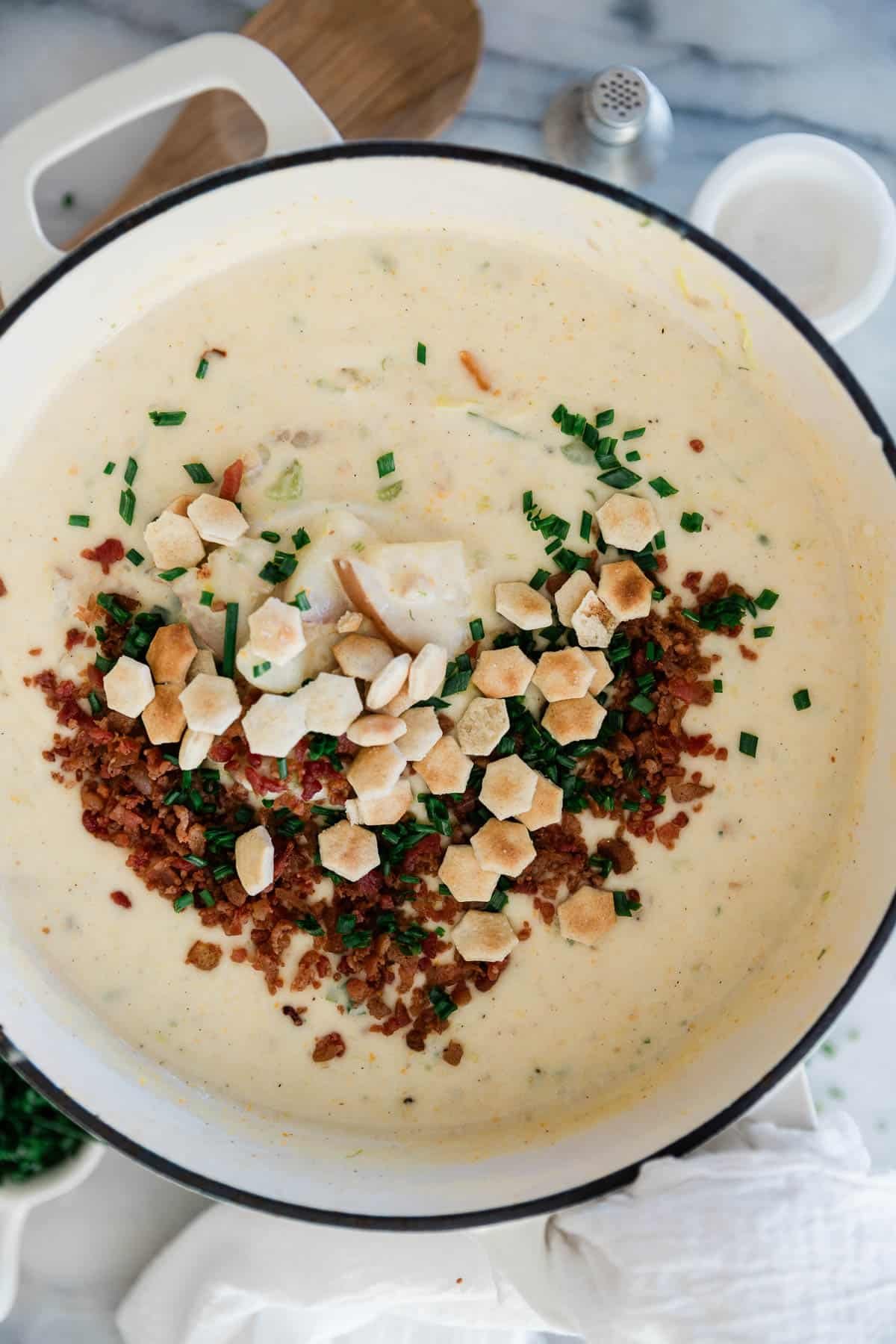 Boston clam chowder in a pot with bacon, oyster crackers, and parsley sprinkled on top.