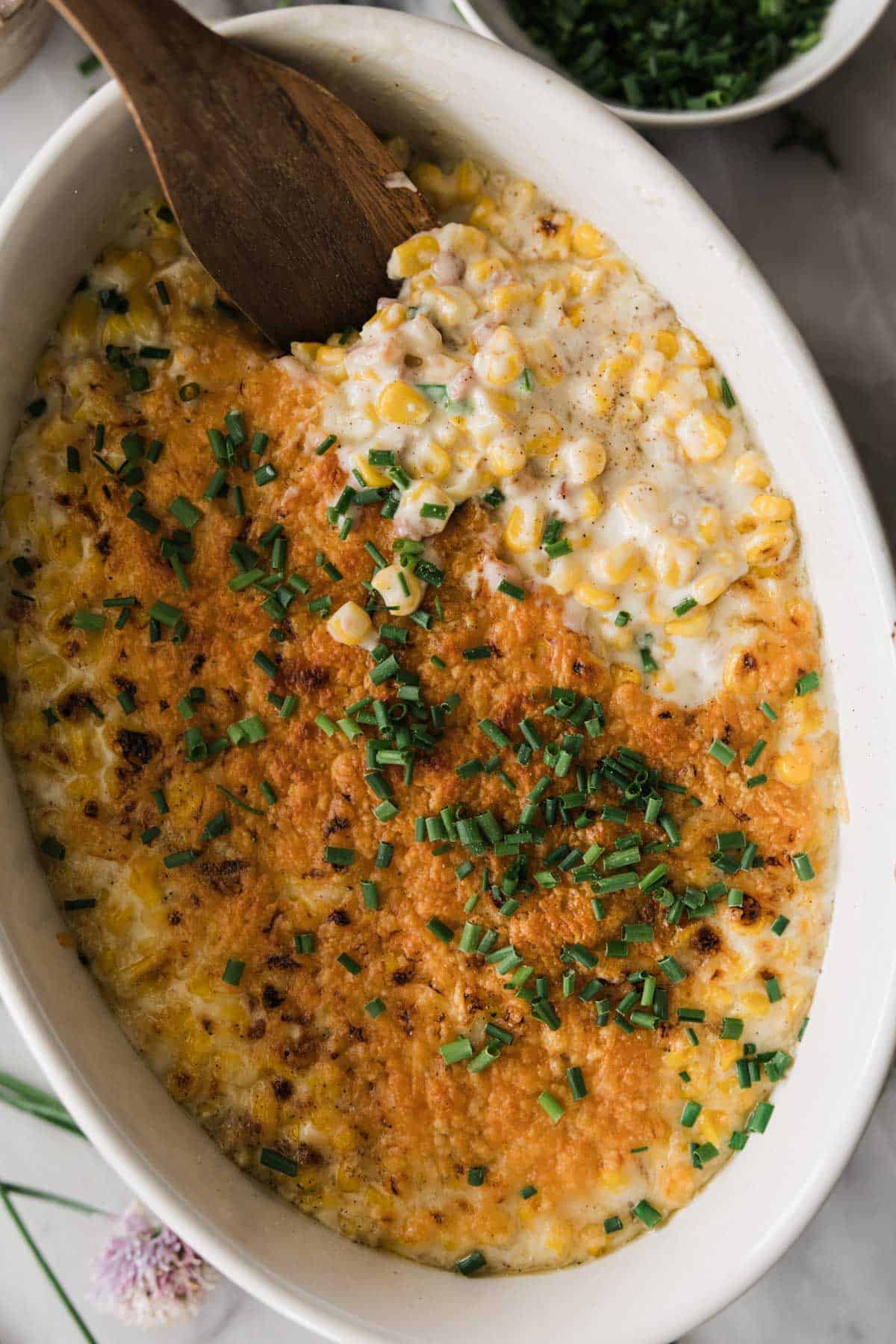 Homemade creamed corn in a serving dish with a wooden spoon resting in the dish. 