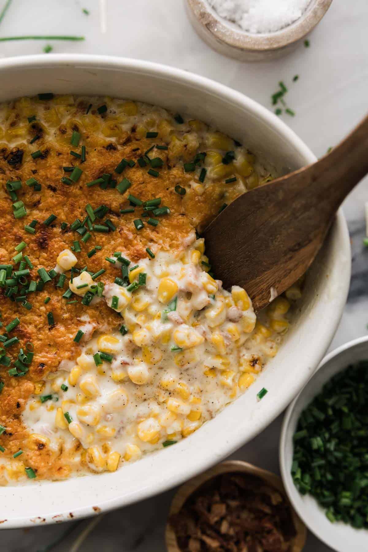 Homemade creamed corn in a serving dish with a wooden spoon scooping up a portion. 
