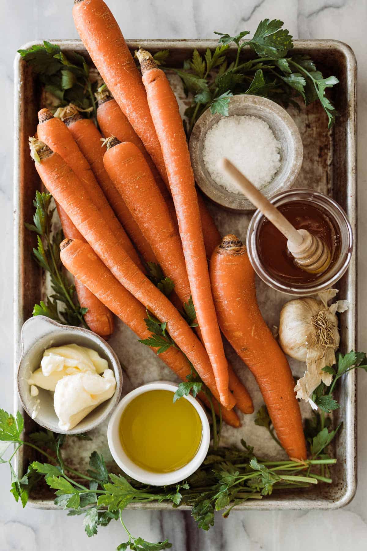 Ingredients for making honey glazes carrots in bowls on a sheet pan.