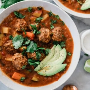 A bowl of Mexican albondigas soup topped with chopped cilantro and slices of avocado.