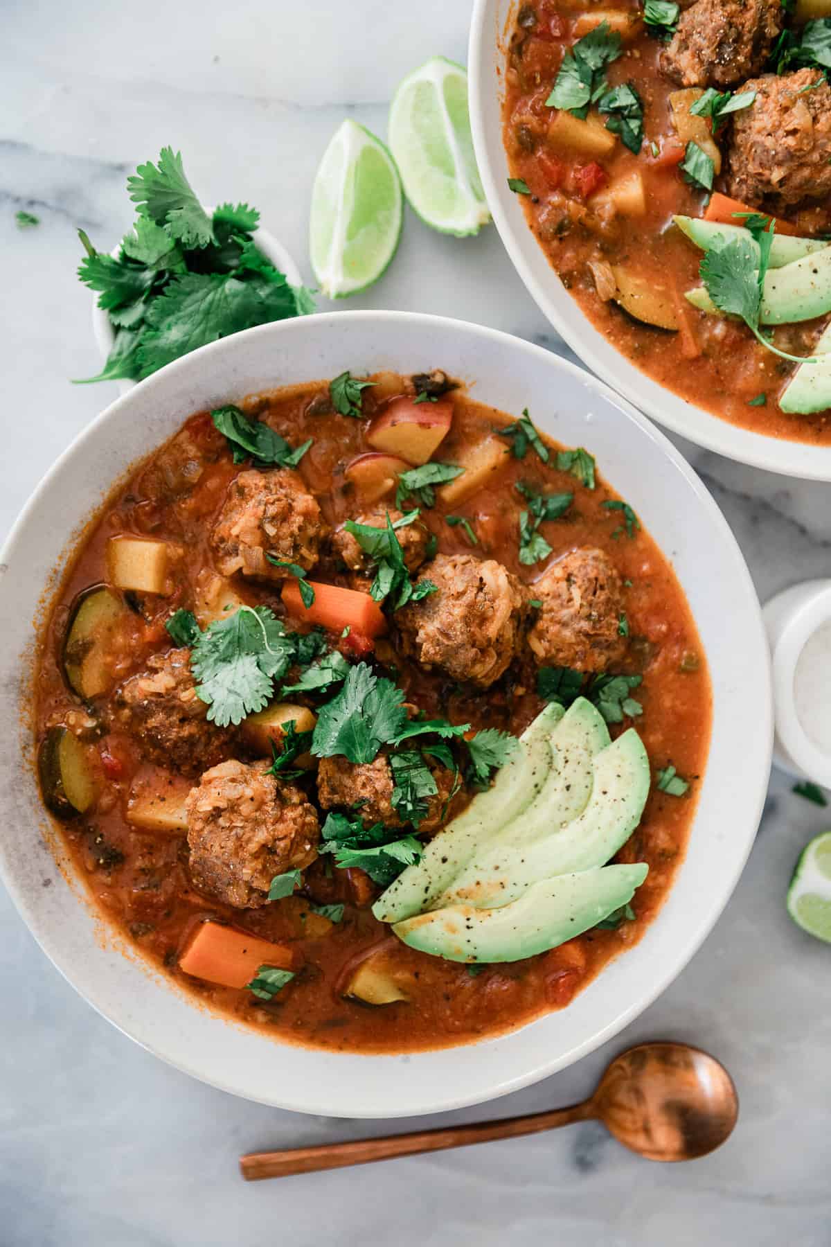 Mexican albondigas soup in bowls with cilantro and lime wedges scattered around.
