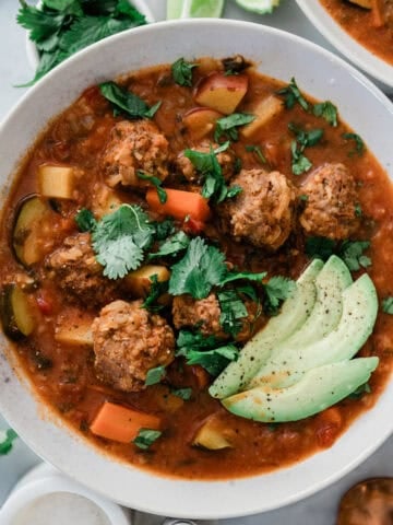 A bowl of Mexican albondigas soup garnished with cilantro and avocado slices.