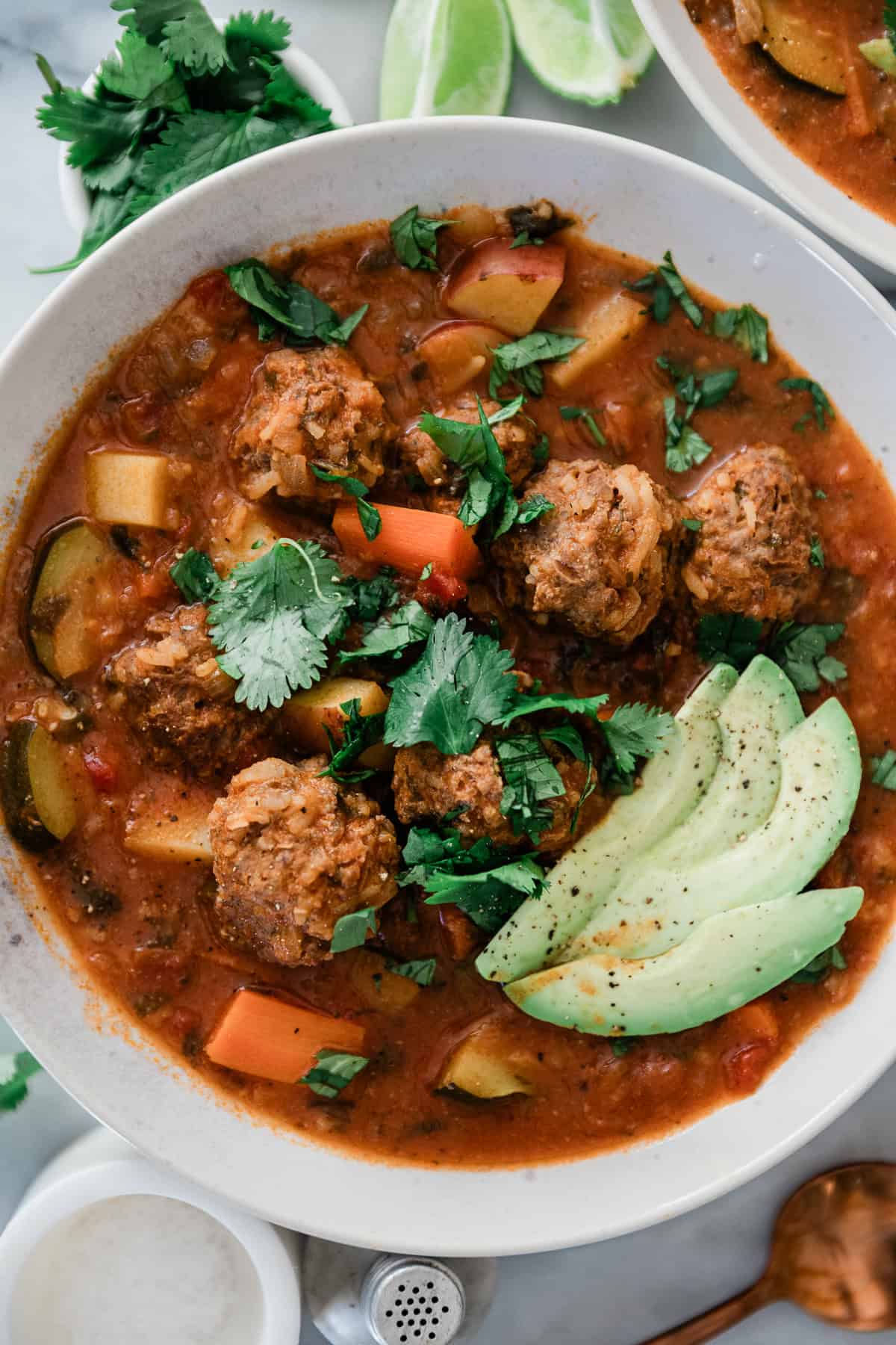 A bowl of Mexican albondigas soup garnished with cilantro and avocado slices.