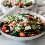 Bowls of Panera black bean soup on a table topped with cheese and avocado.