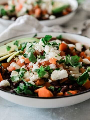 Bowls of Panera black bean soup on a table topped with cheese and avocado.