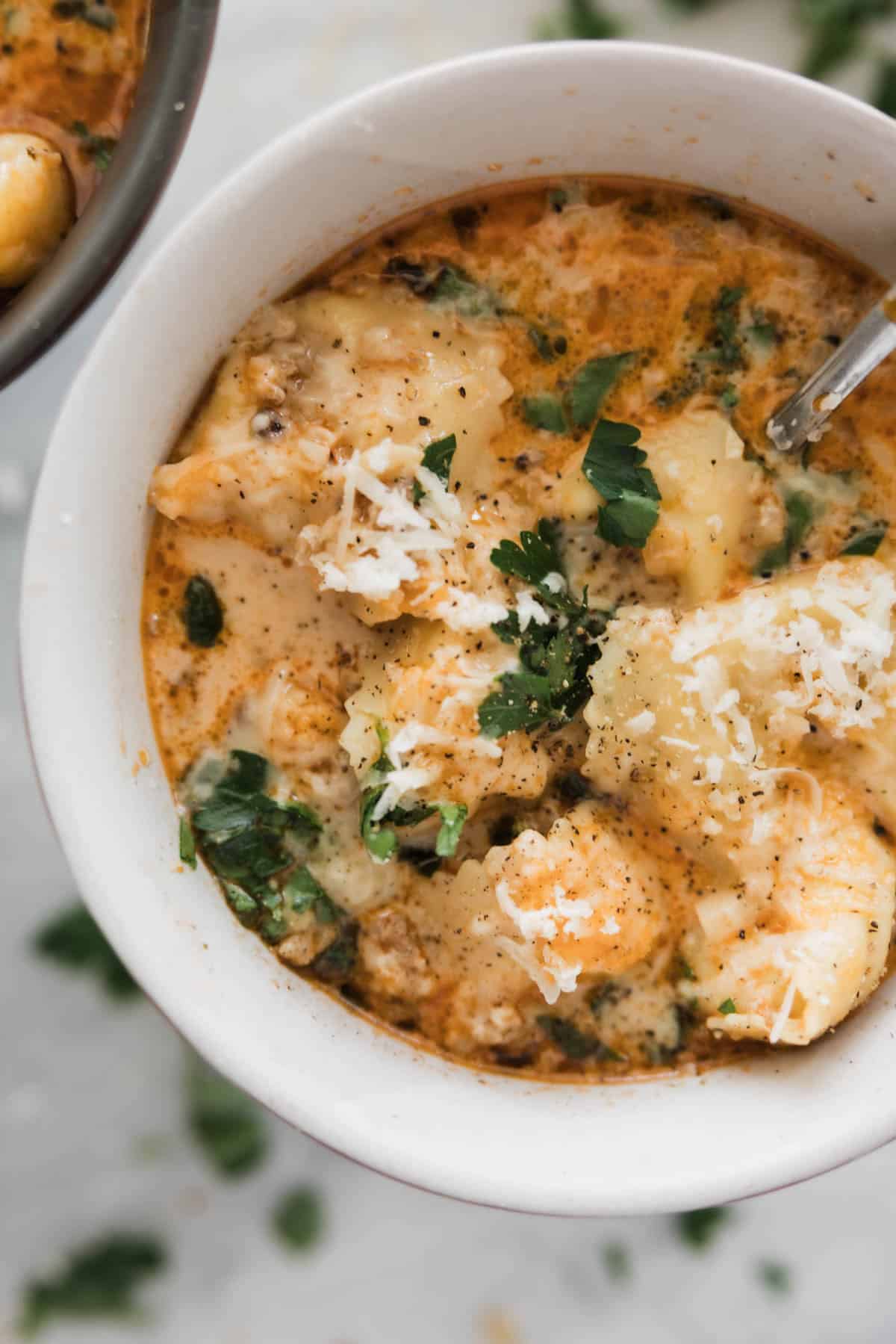 A bowl of tortellini soup with sausage garnished with fresh herbs. 