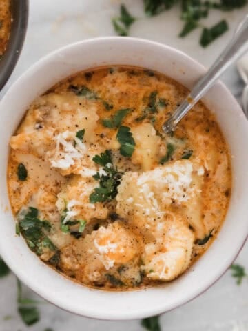 A bowl of sausage tortellini soup with a spoon in the bowl.