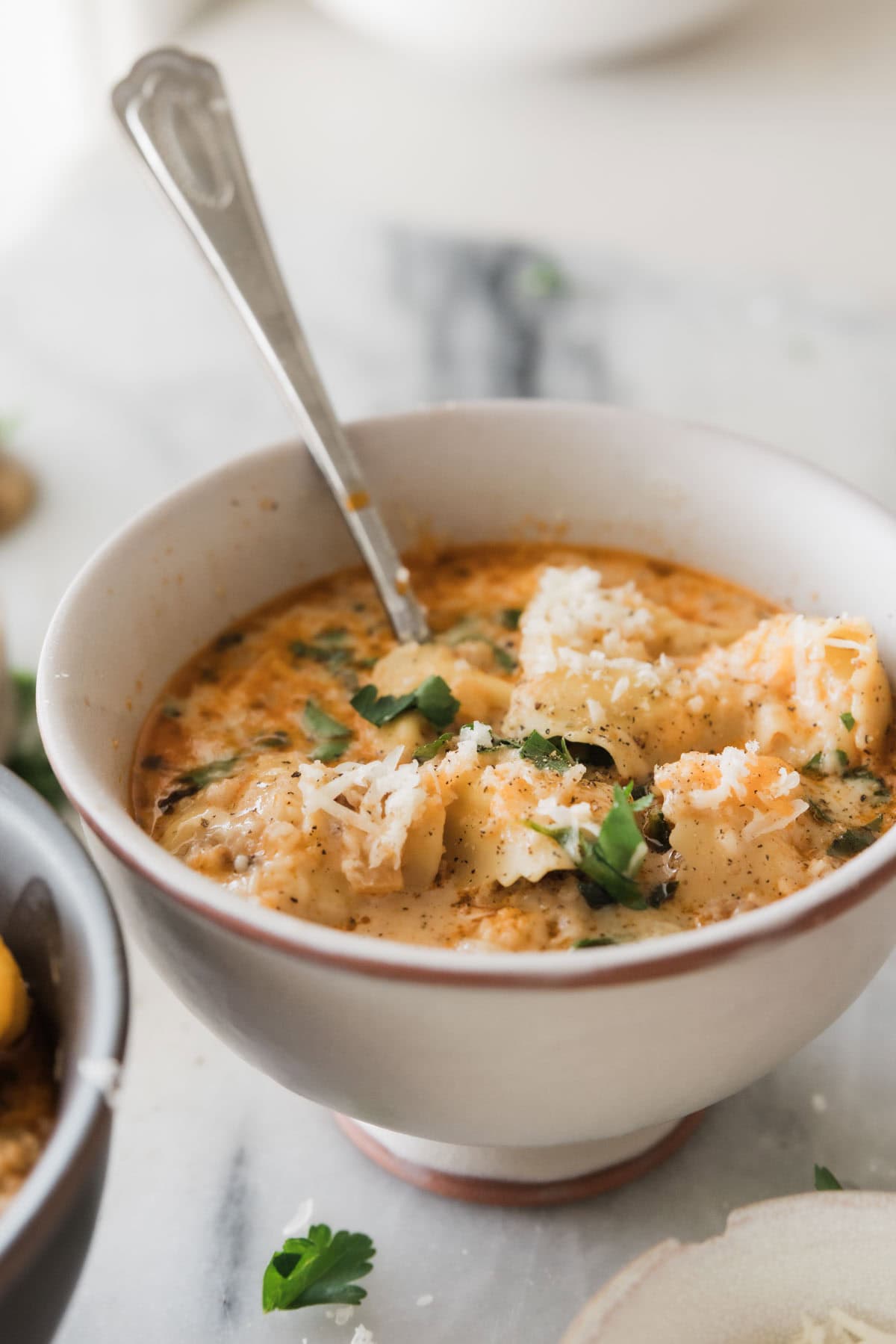 A bowl of sausage and tortellini soup with a spoon in the bowl. 