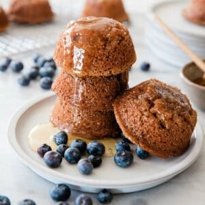 Raisin bran muffins stacked on a plate with blueberries on the side.