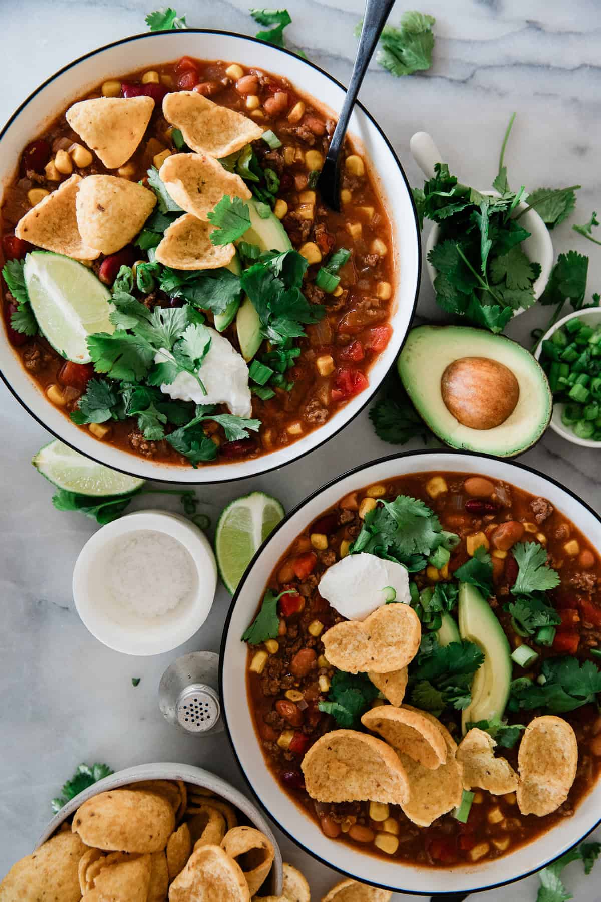 Two bowls filled with taco soup and avocados and lime scattered around the bowls.