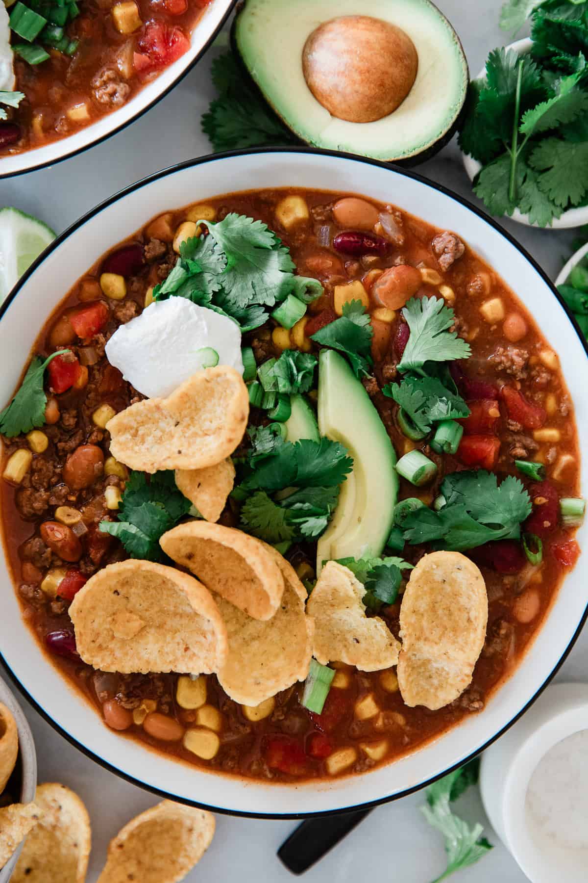 A bowl of taco soup topped with corn chips, avocado, cilantro and sour cream.
