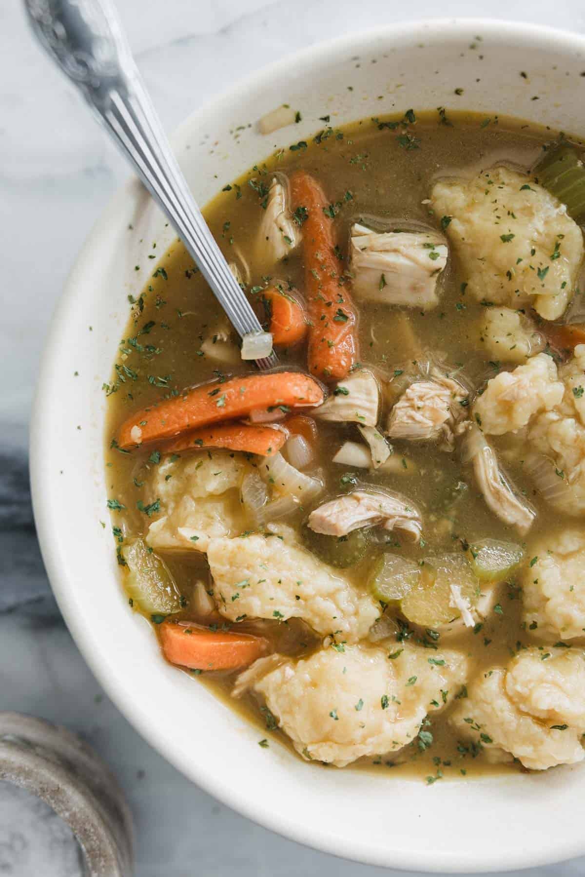 A bowl filled with chicken, dumplings, and vegetables with a spoon.