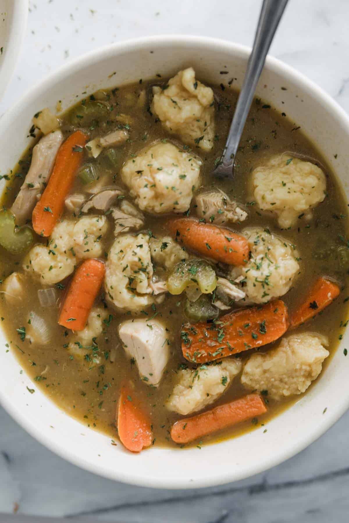 Chicken dumpling soup recipe in a bowl with a spoon resting to the side. 