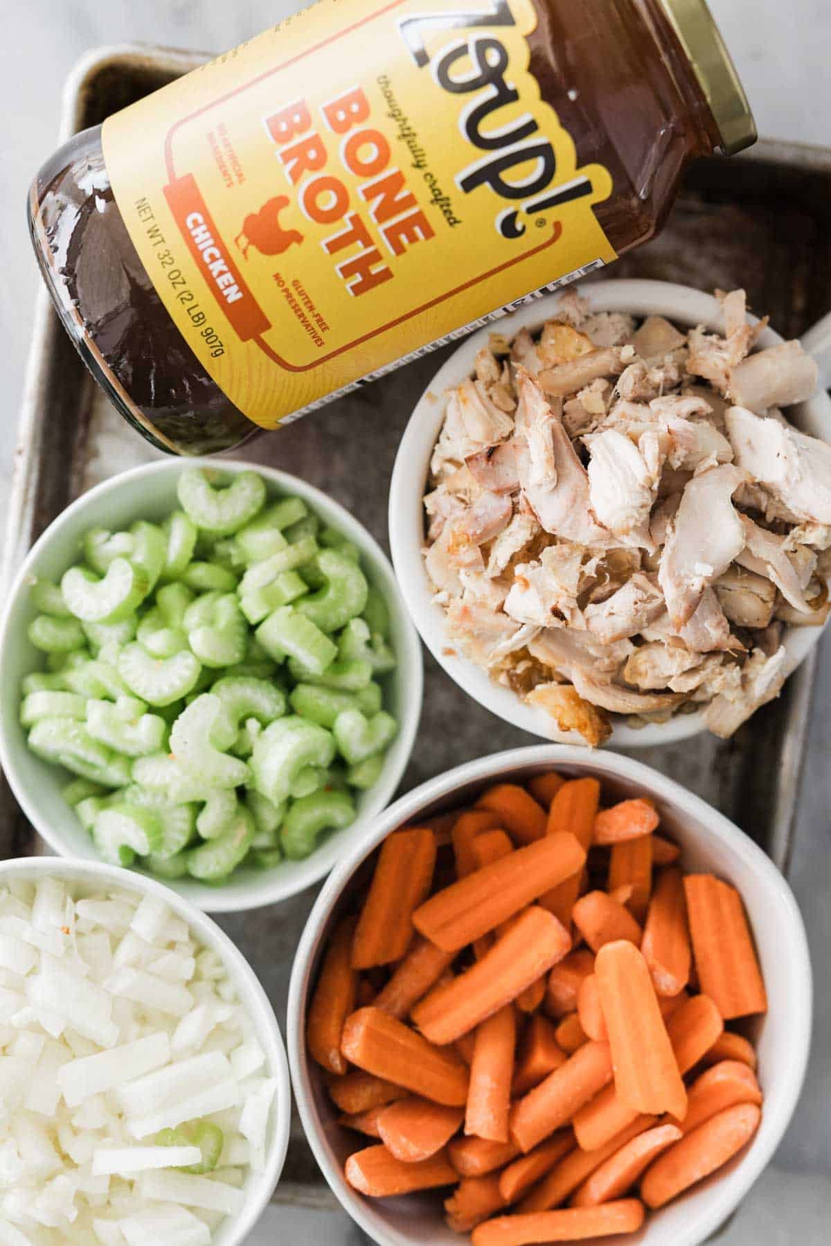 Ingredients to make this chicken and dumpling soup in bowls on a table.