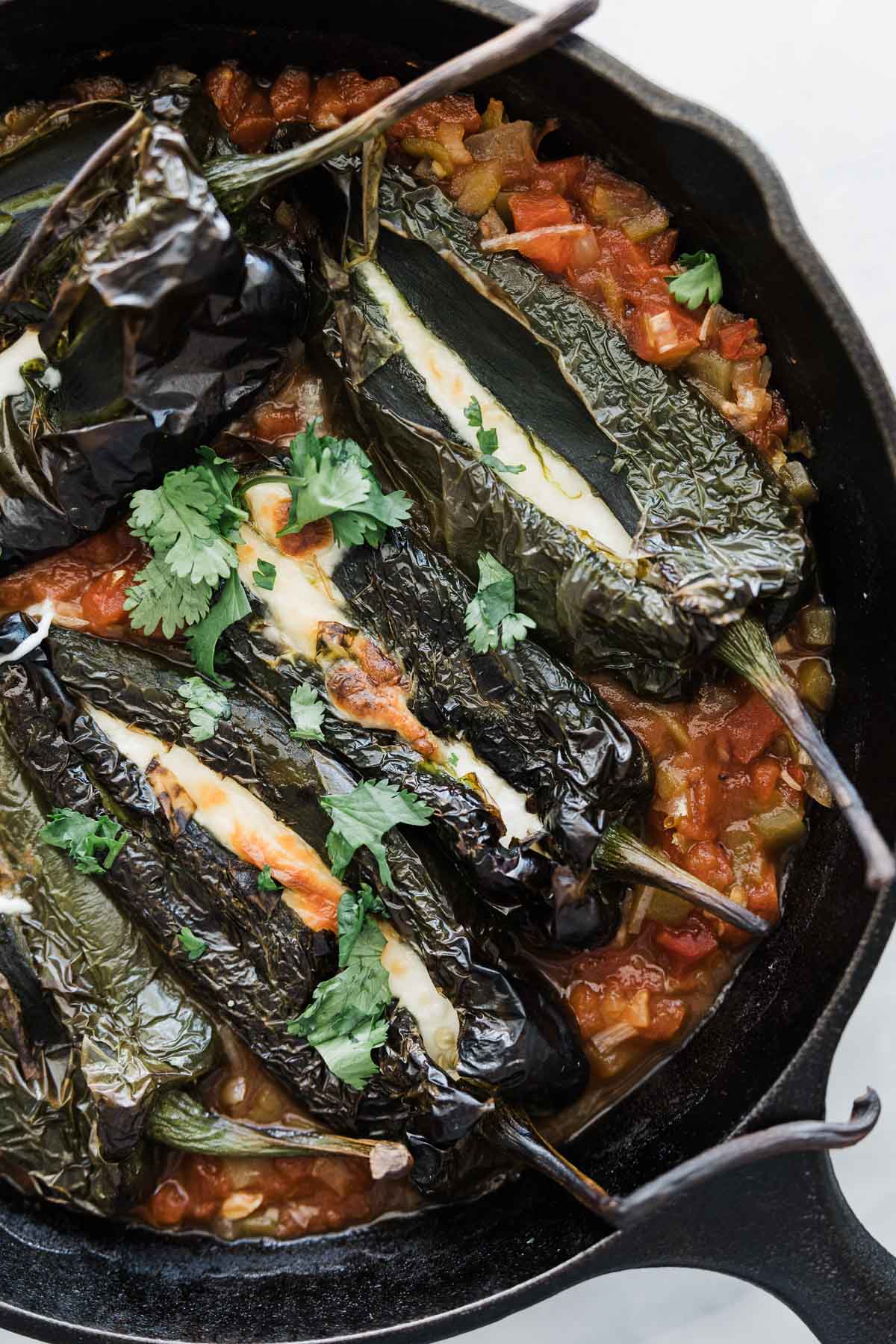 A cast iron pan with chile rellenos in salsa.