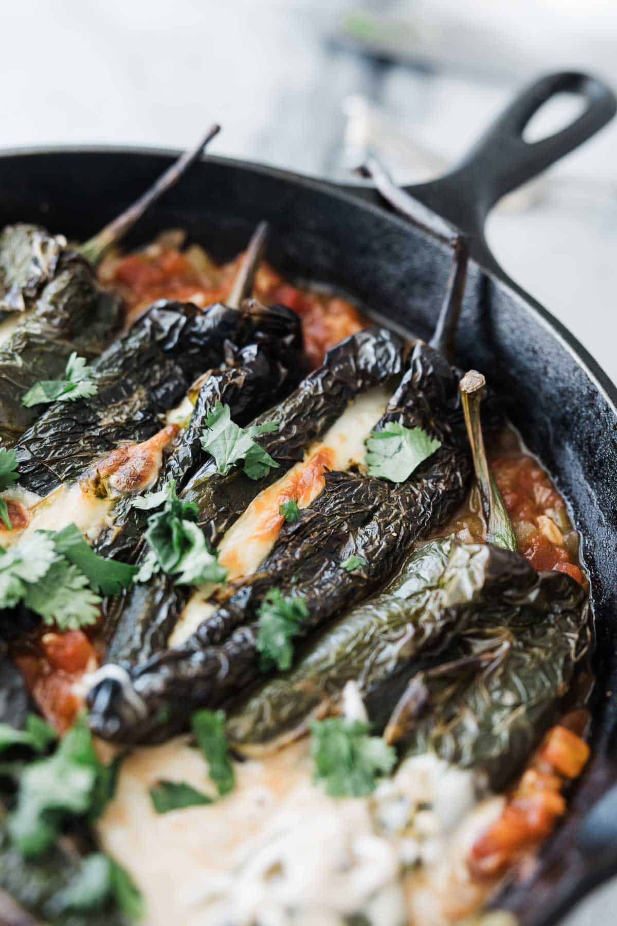 A bunch of chile rellenos with tomato salsa in a skillet. 
