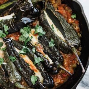 Chile rellenos stuffed with onions and cheese in a skillet.