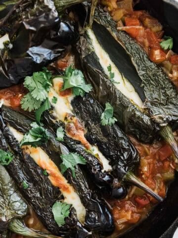 Chile rellenos stuffed with onions and cheese in a skillet.