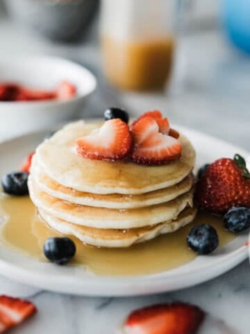A stack of panakes with strawberries and coconut syrup on top.